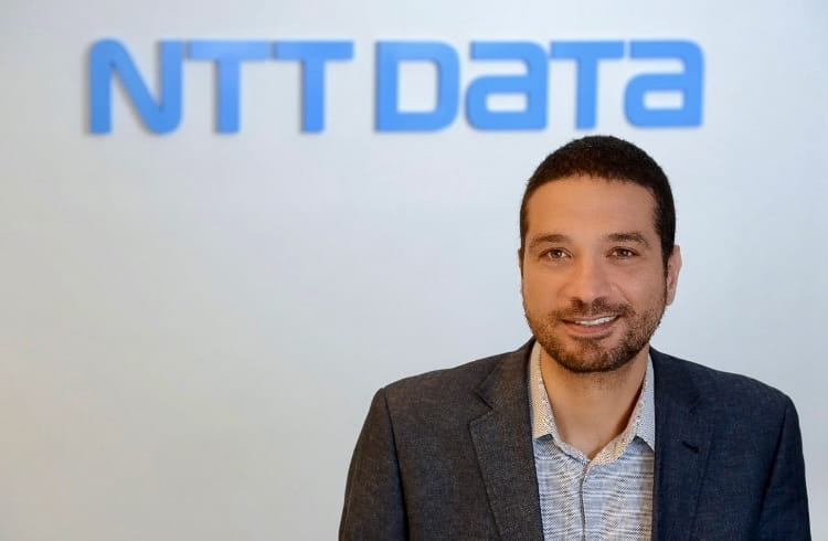 un hombre con un traje de pie frente al logotipo de datos de NTT