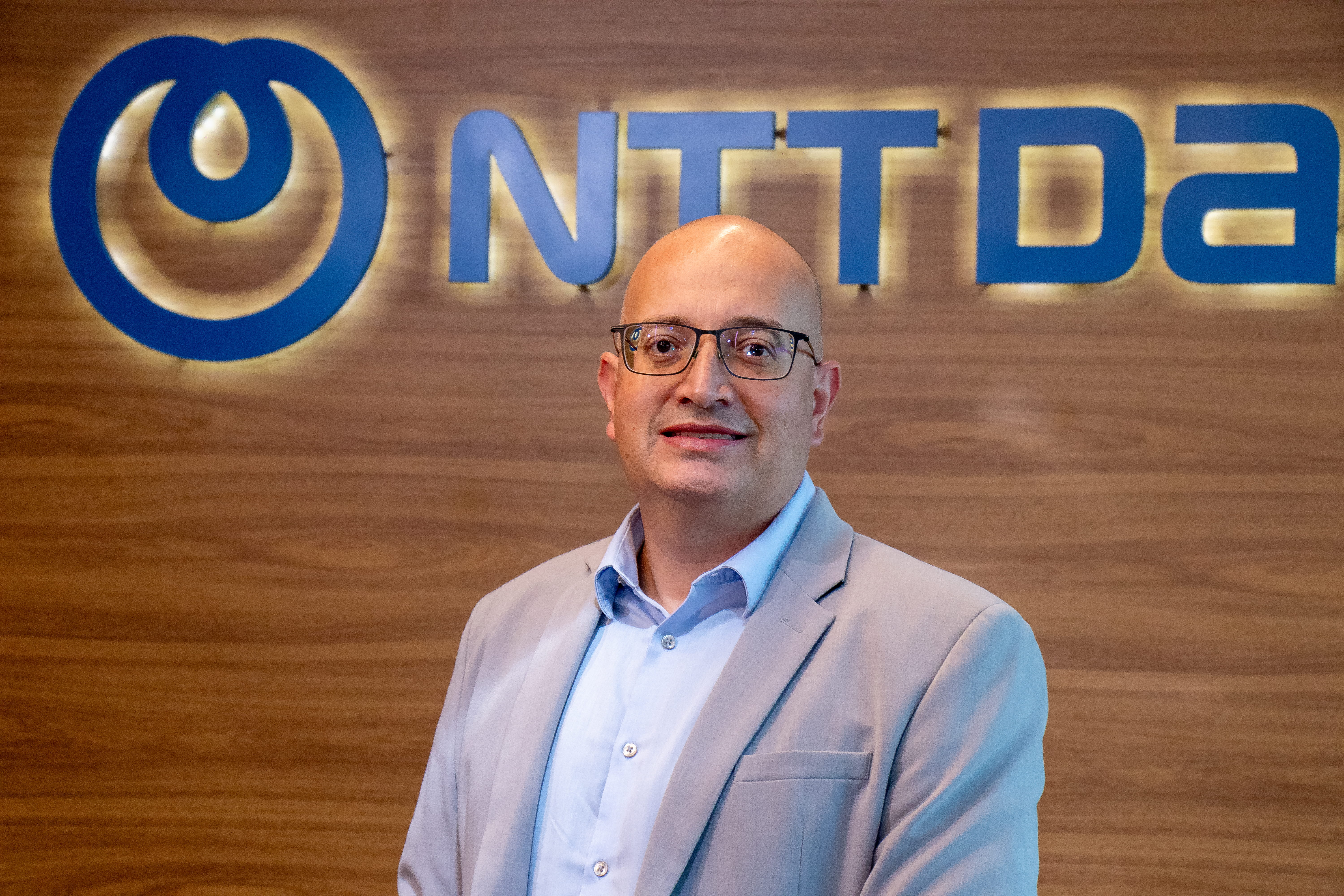 Thales Cyrino sorrindo para foto com logo NTT DATA ao fundo