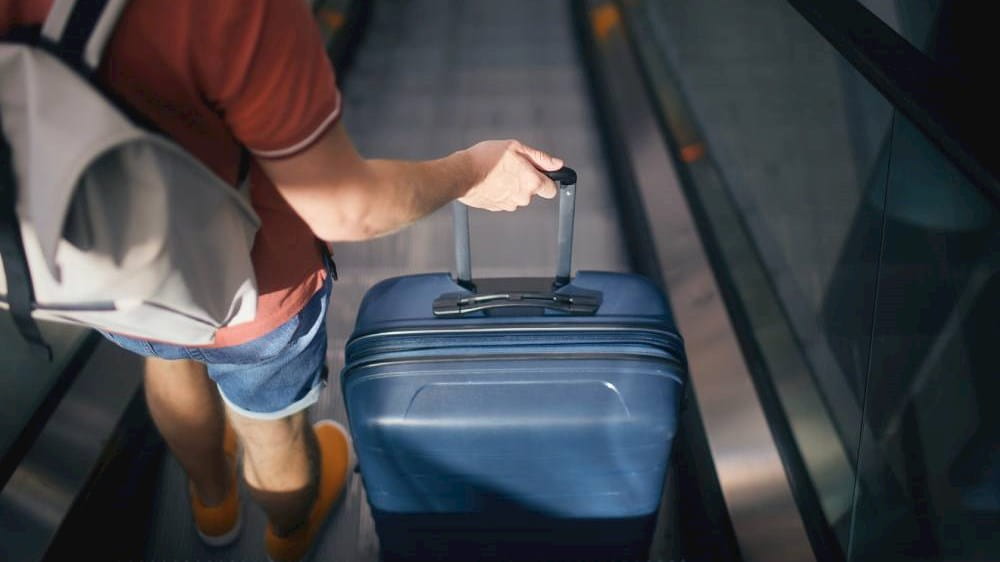 rear-view-of-man-with-suitcase-and-backpack-on-esc