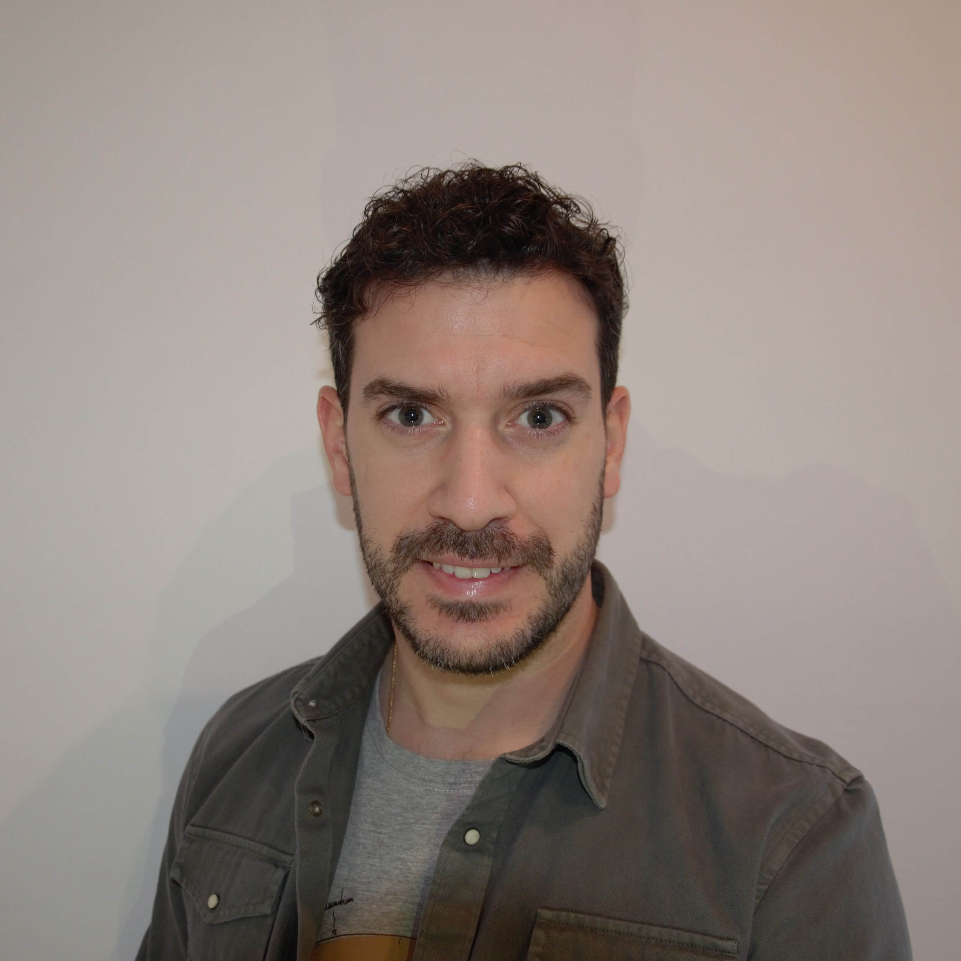 Un hombre con una camisa gris parada frente a una pared blanca