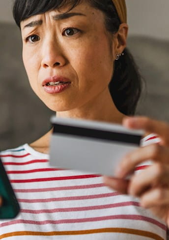 Donna guarda preoccupata lo smartphone mentre cerca di pagare online con la carta