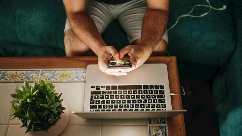 Persona vista dall'alto scrive con lo smartphone mentre è seduta davanti al pc