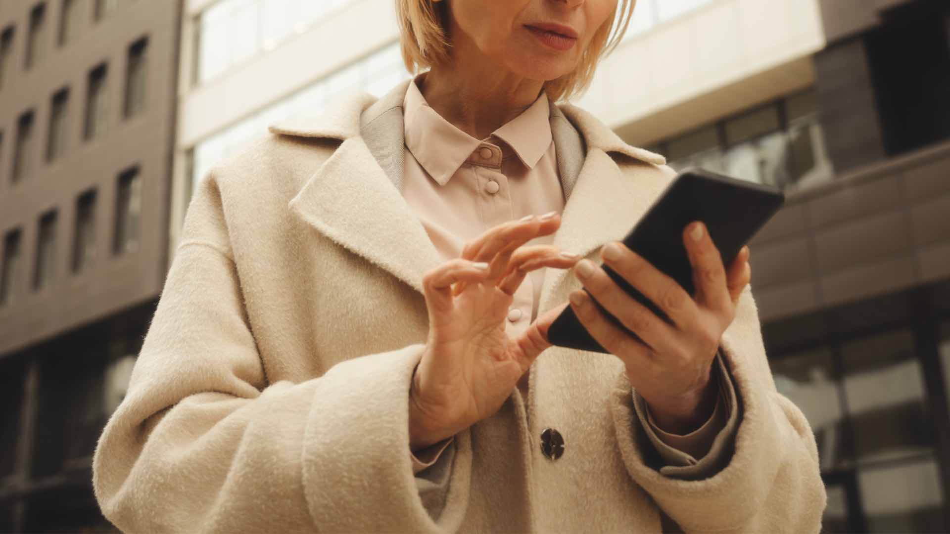 Donna con cappotto bianco e smartphone in mano