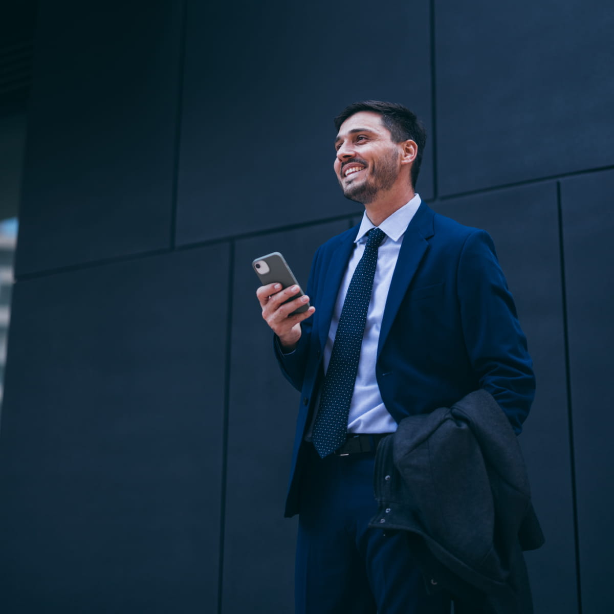 Uomo in giacca e cravatta con cellulare in mano guarda verso l'alto