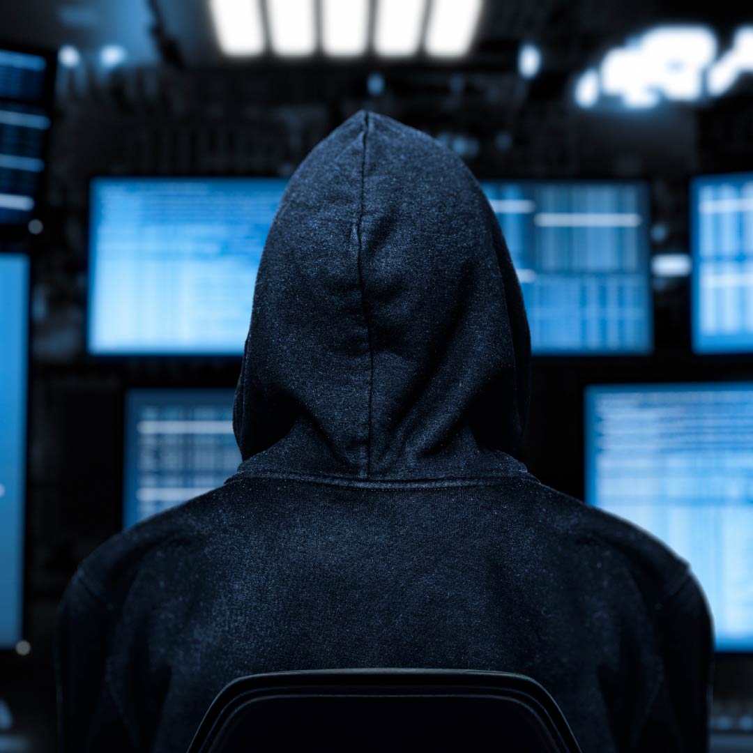Hacker incappucciato di spalle davanti a schermi del computer