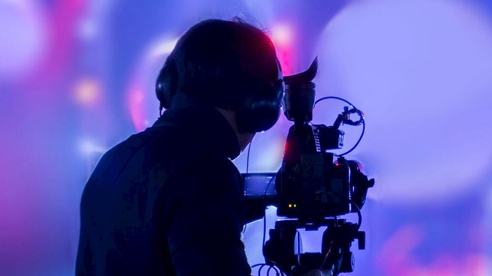Cameraman visto di spalle su sfondo blu e viola_Wp NTT DATA Video Solutions Smart Operations