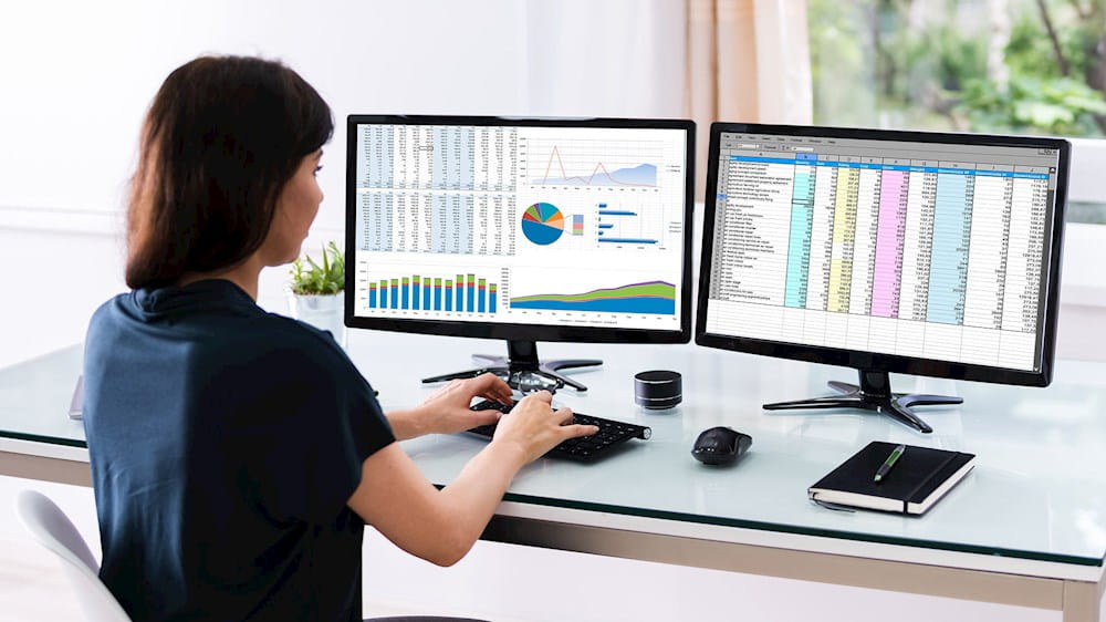 a woman working at a desk with two monitors