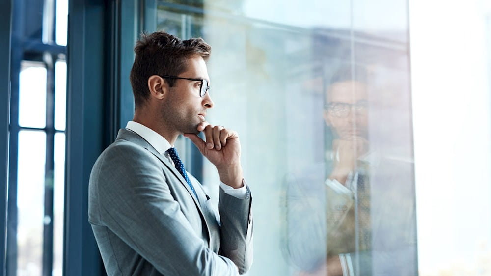 Homem em traje de negócios a olhar por uma janela