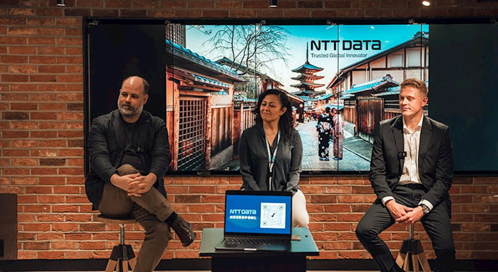 three people sitting on stools in front of a screen