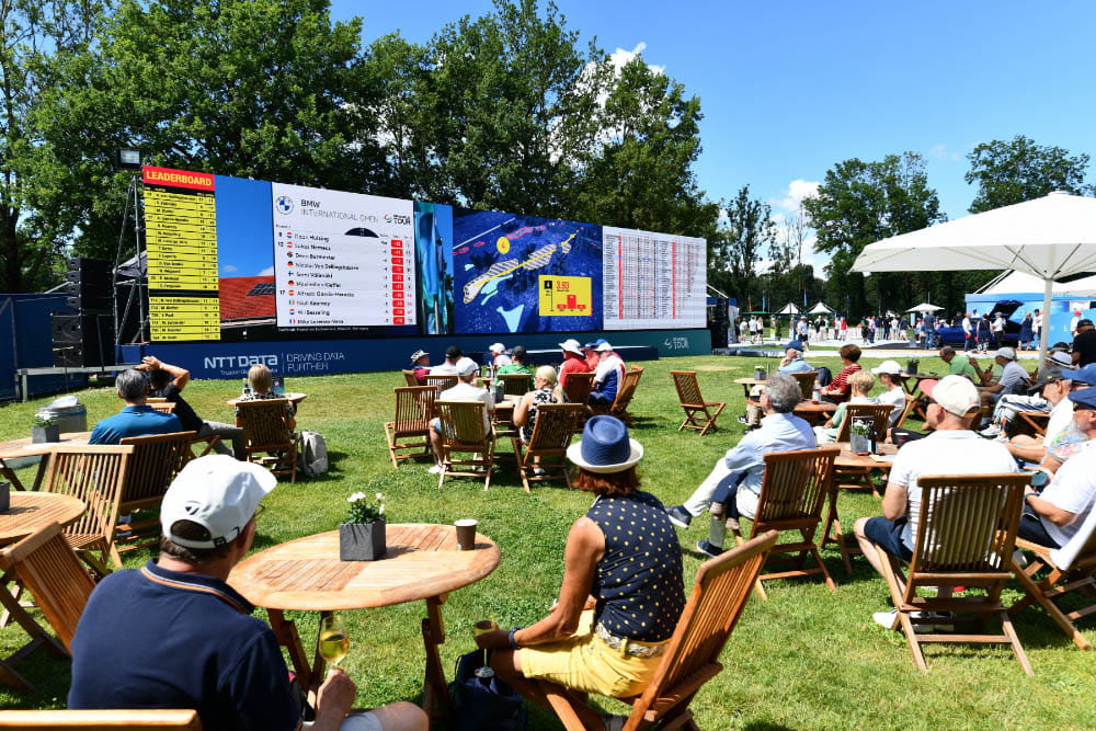 a group of people watching a golf tournament on a large screen