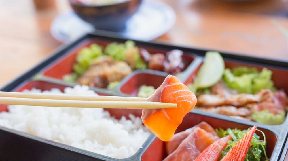 a bento box with sushi, rice, and chopsticks