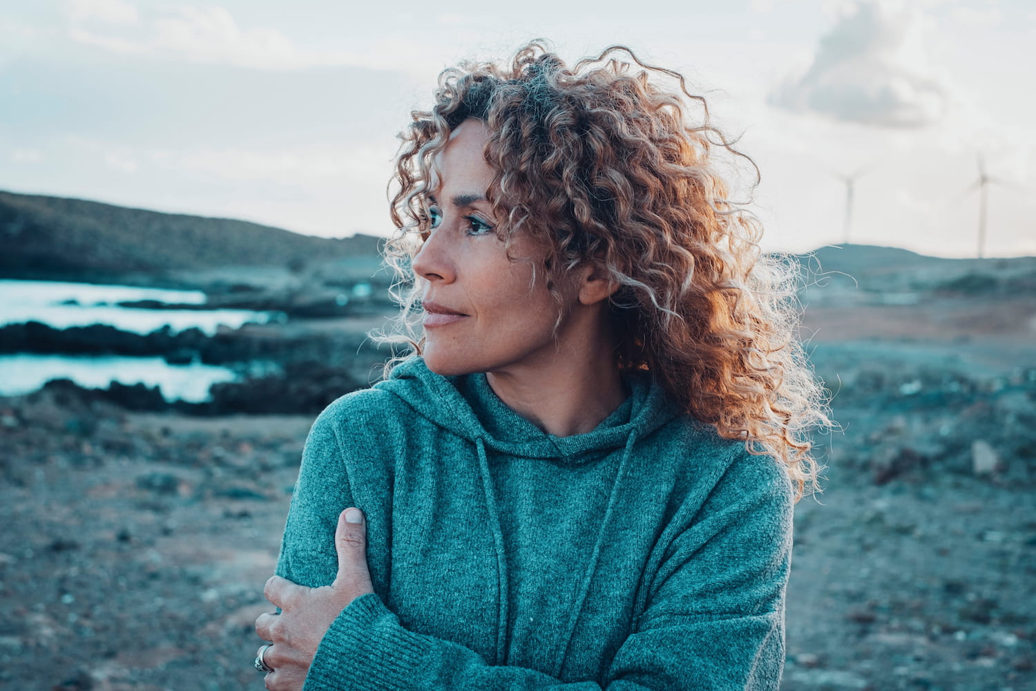 a woman with curly hair standing in front of wind turbines