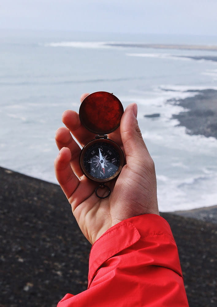 a person holding a compass in front of the ocean