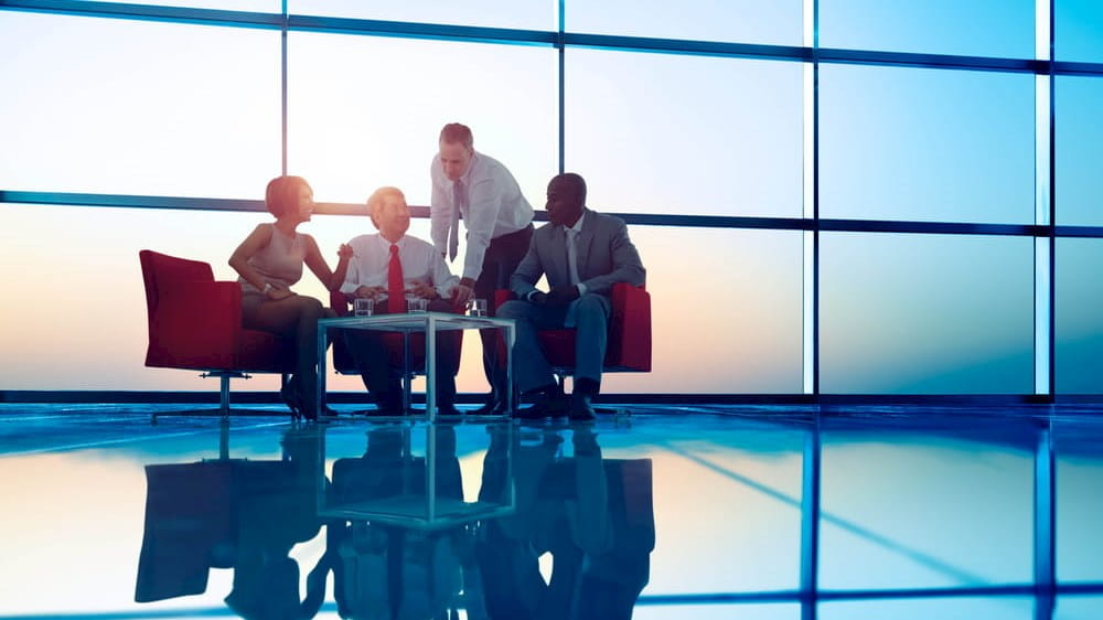 a group of business people sitting around a table in front of a large window