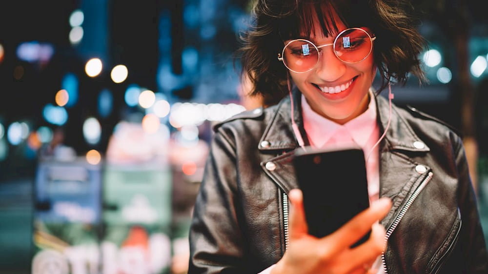 a woman wearing sunglasses and a leather jacket looking at her phone