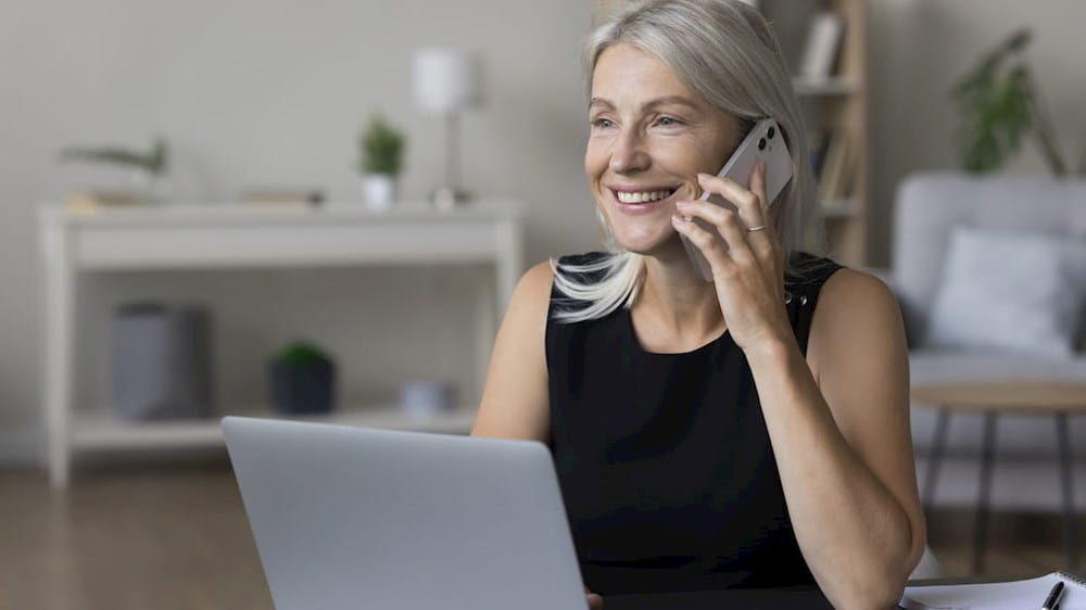 a woman talking on the phone while sitting in front of a laptop