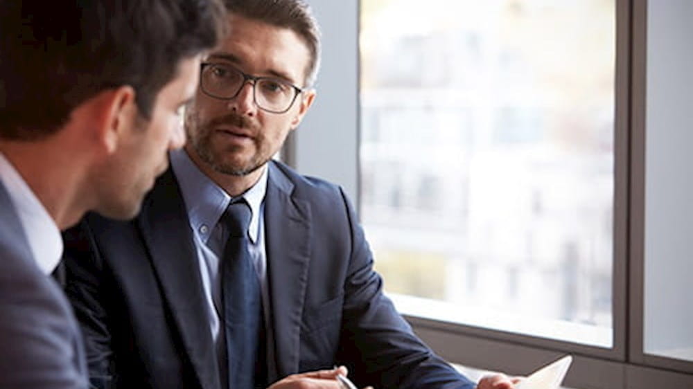 Two businessmen are sitting at a table and talking to each other